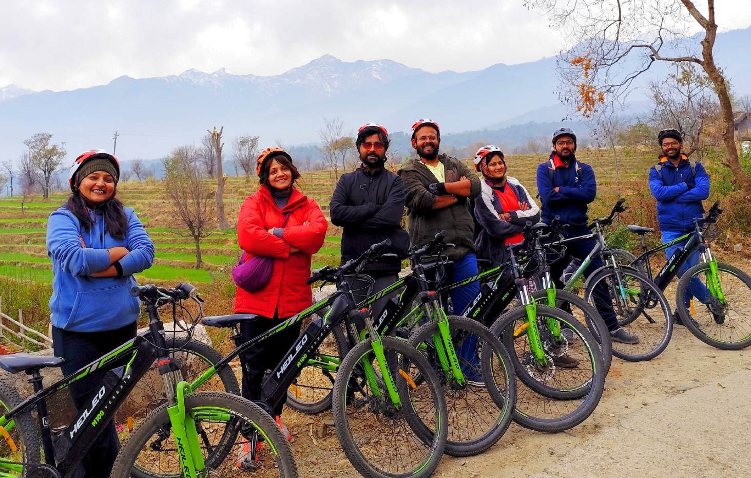 Group of riders with e‑cycles, Dhauladhar range and terraced fields behind